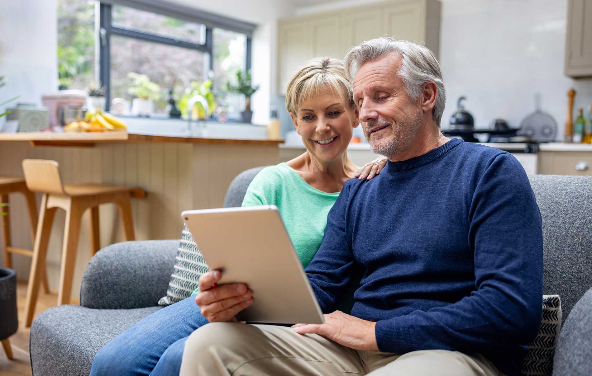 Couple smiling as they look at a tablet together on the couch at home