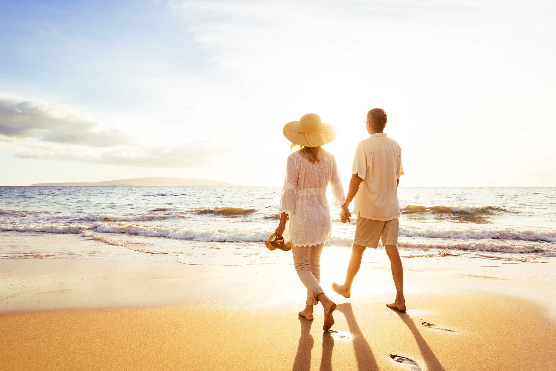 Retired couple walking hand in hand along the beach at sunset