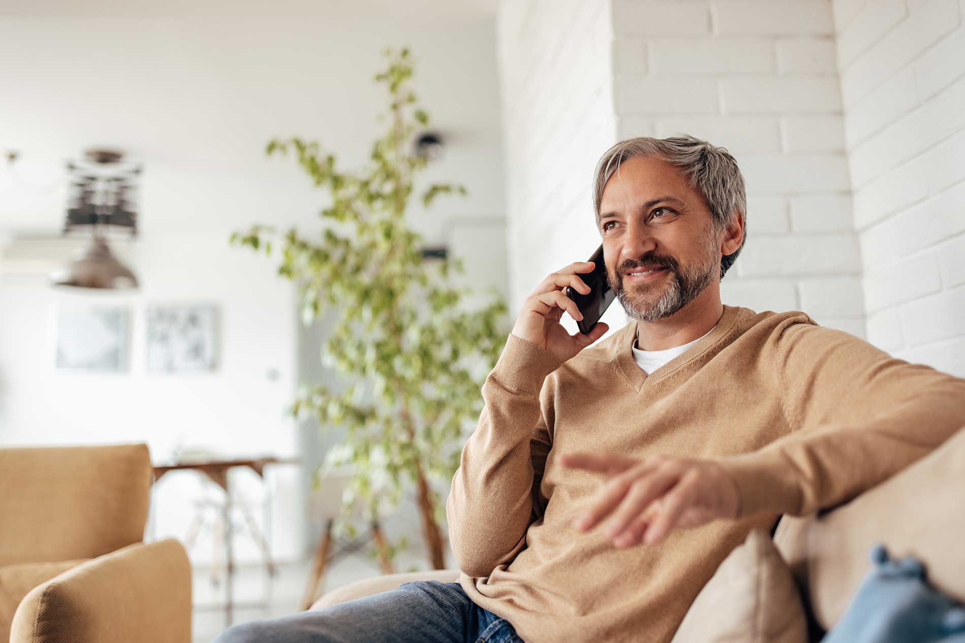 Smiling man relaxing on the couch at home while talking on the phone