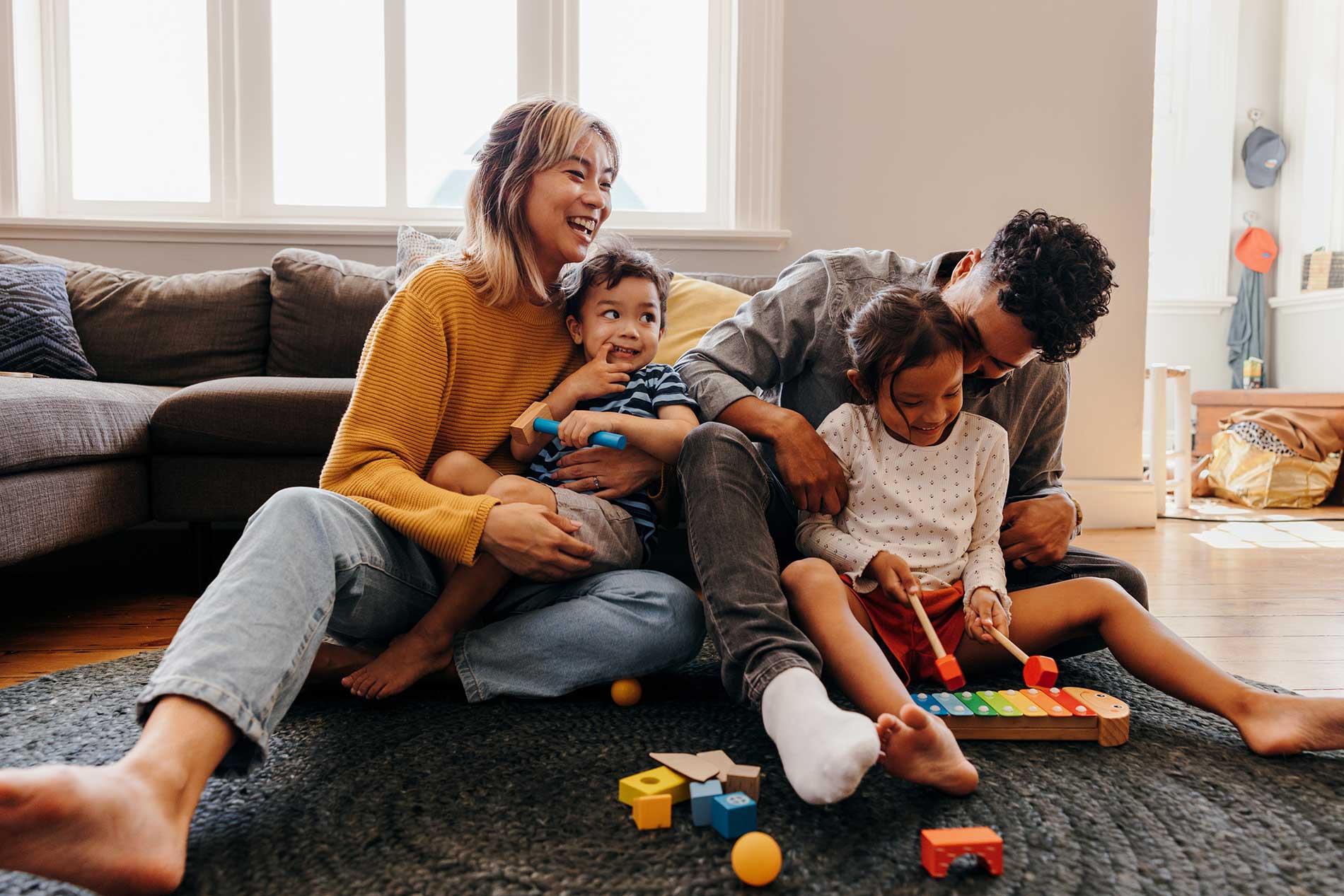 Parents laughing with their two young children while playing on the living room floor at home