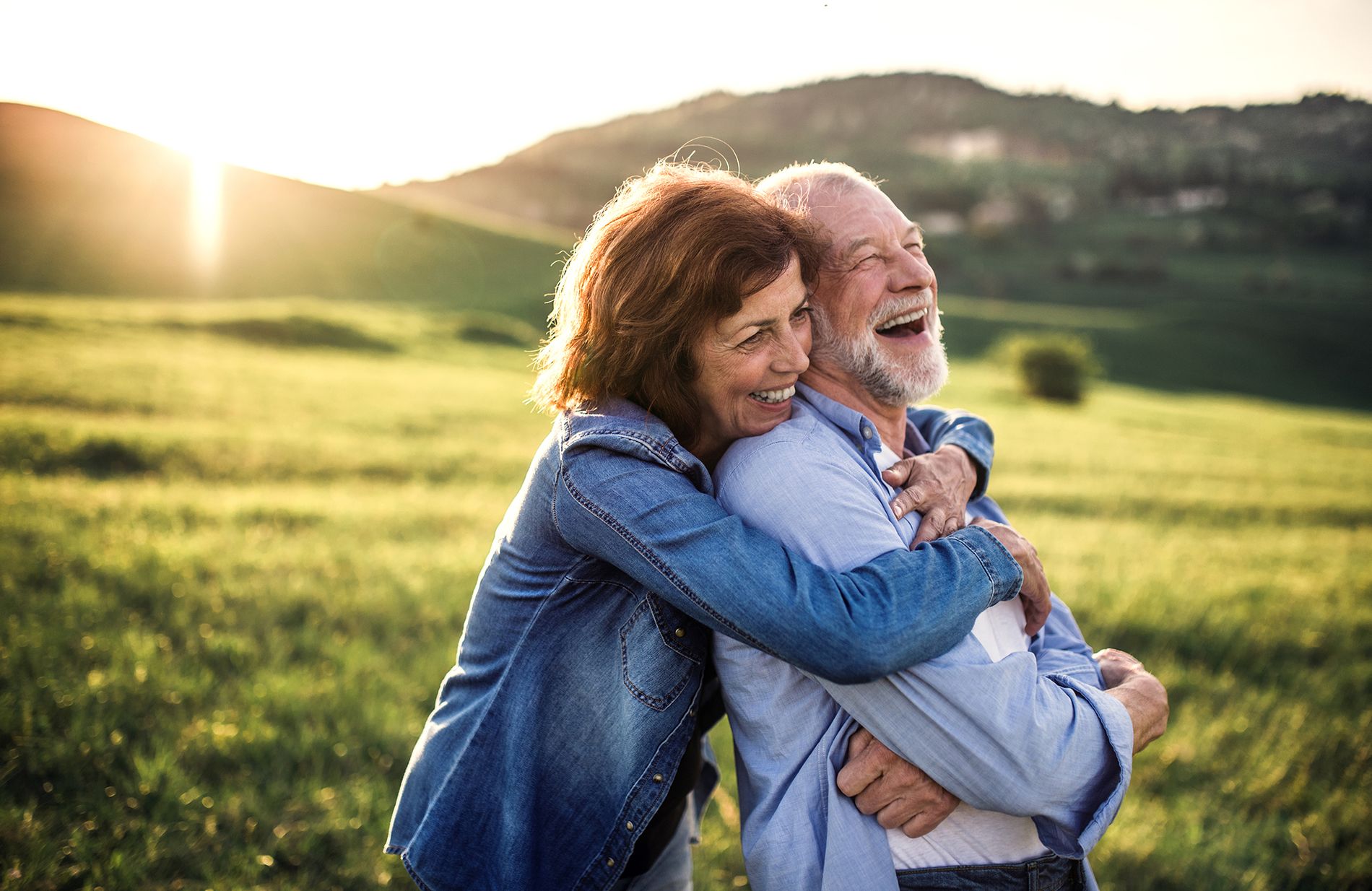 Laughing retired couple embracing in a sunny field