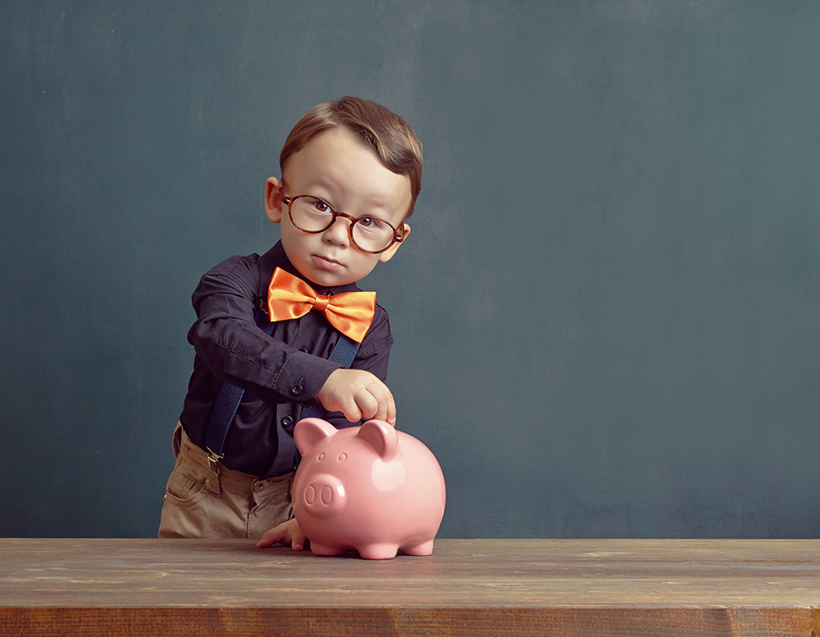 Young boy in glasses and a bow tie putting a coin into a piggy bank
